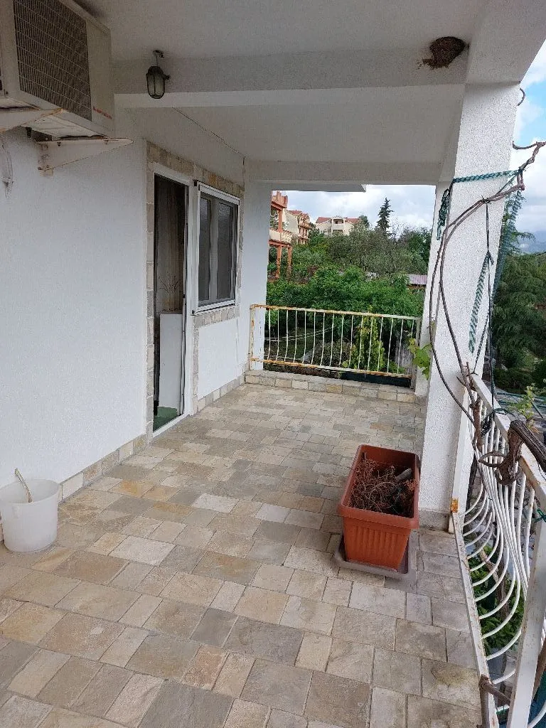 Natkrivena terasa sa popločanim podom i pogledom na zelenilo.