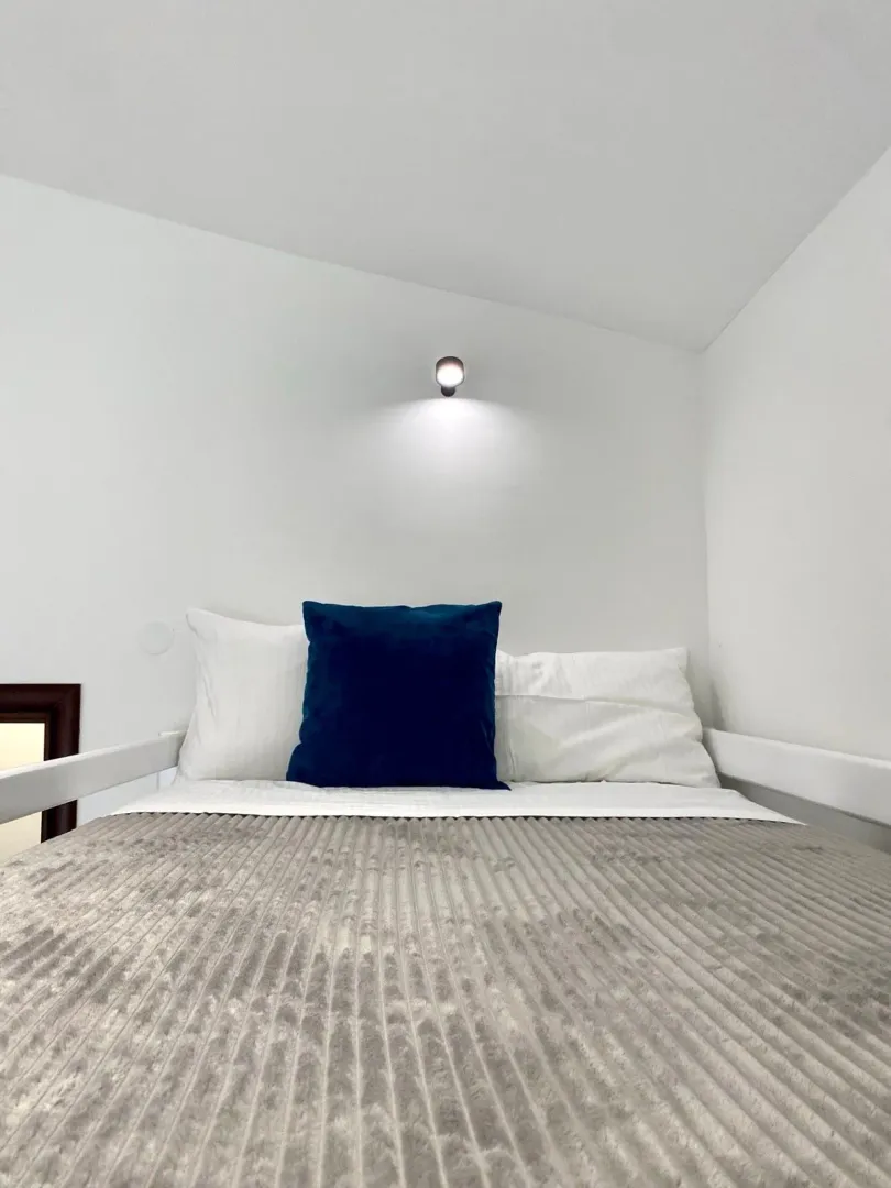 View of the bed in a bedroom with white walls.