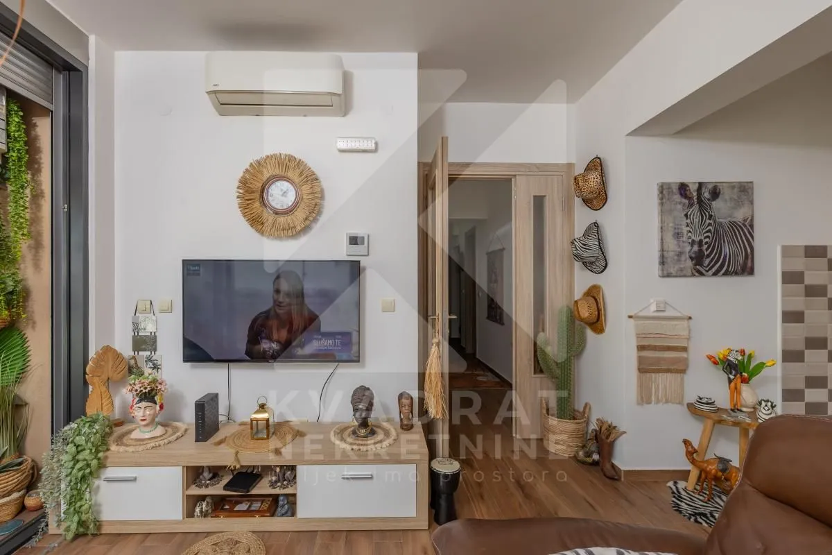 Dnevna soba sa televizorom, namještajem i dekorativnim detaljima.