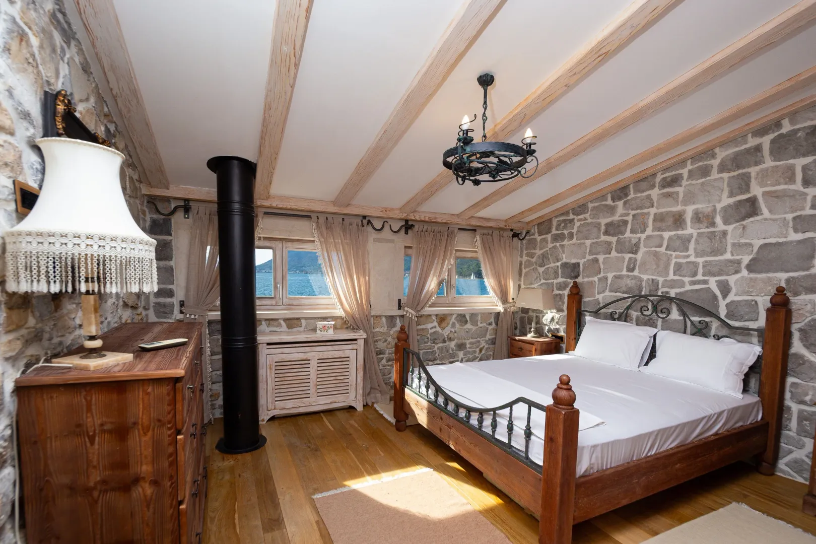 Rustic bedroom with a wooden bed, stone walls, and a sea view.