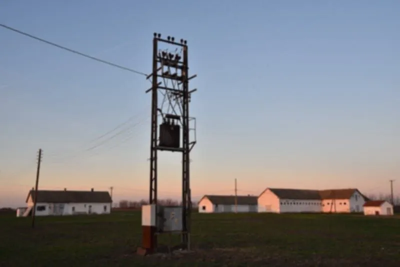 Pogled na eksterijer seoskog imanja sa poljskim objektima i stubom električne mreže.