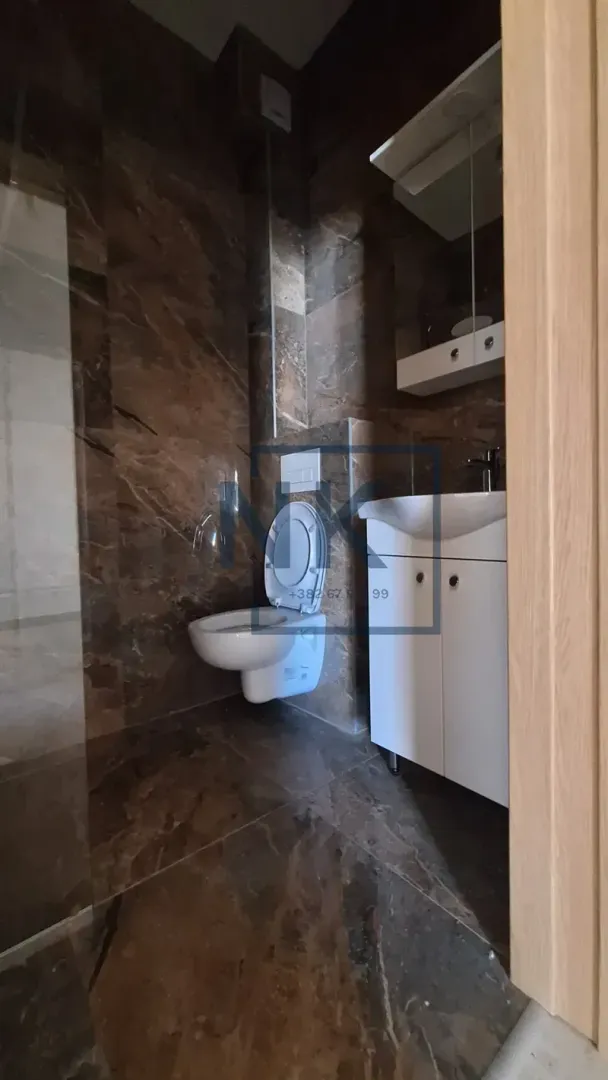 Kupatilo obloženo tamnim pločicama sa WC šoljom i umivaonikom.