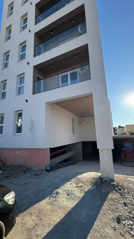 Pogled na spoljašnjost stambene zgrade sa balkonima i ulazom u garažu.