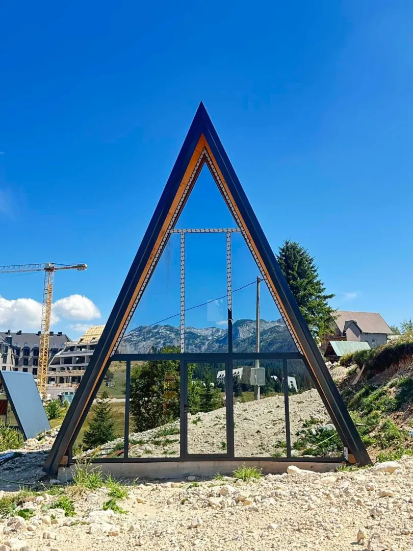 Eksterijer A-frame kuće sa velikim staklenim prozorima u izgradnji.