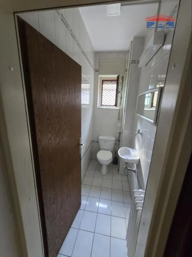 Smaller bathroom with white tiles, washbasin and toilet bowl.