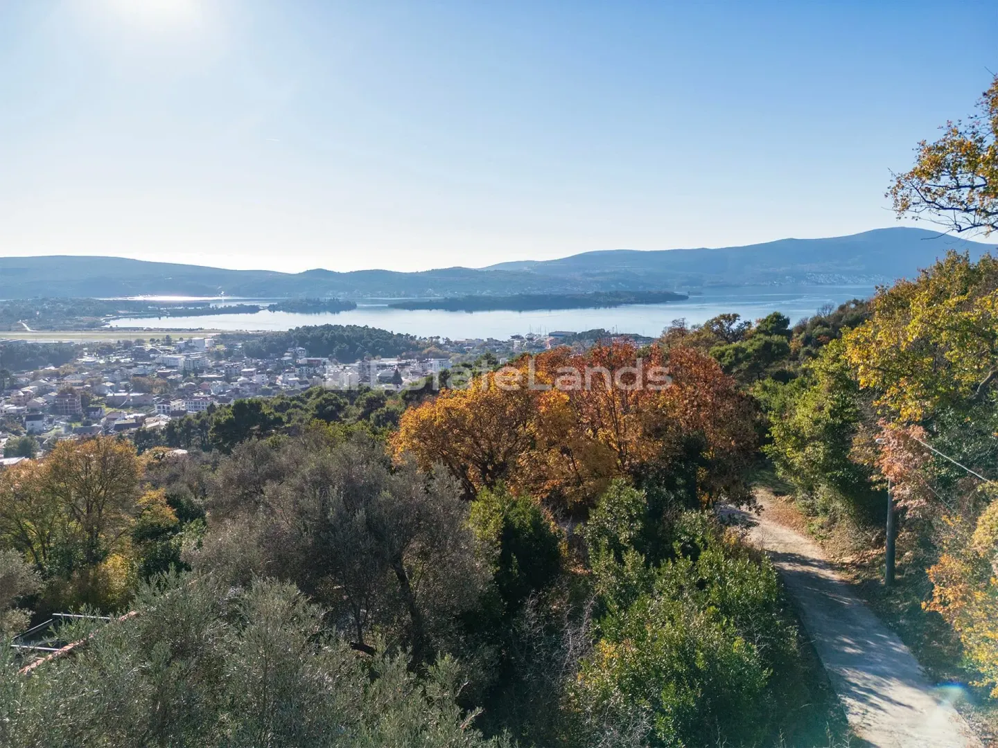Pogled na more i okolno naselje sa zelenilom u prvom planu.