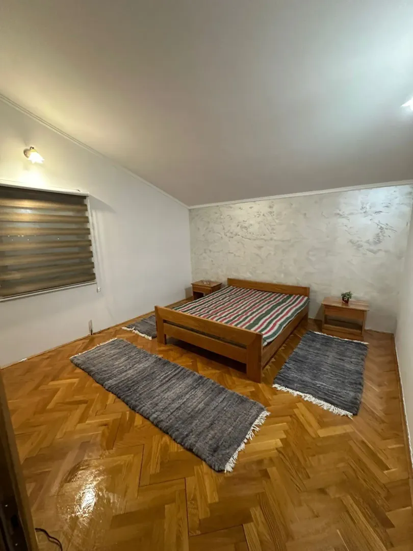 A simply furnished bedroom with a wooden bed and parquet flooring.