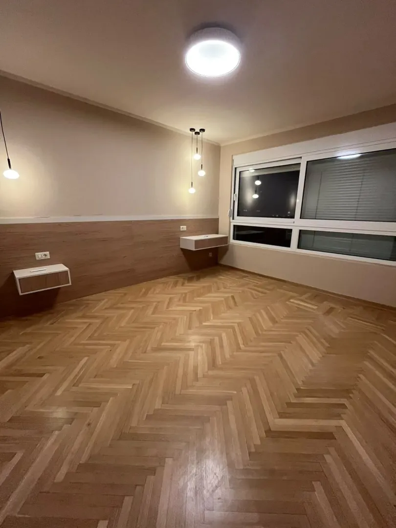 Prazna spavaća soba sa drvenim parketom i ugradnim noćnim stočićima.