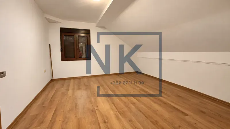 Empty attic room with wooden flooring and a window.