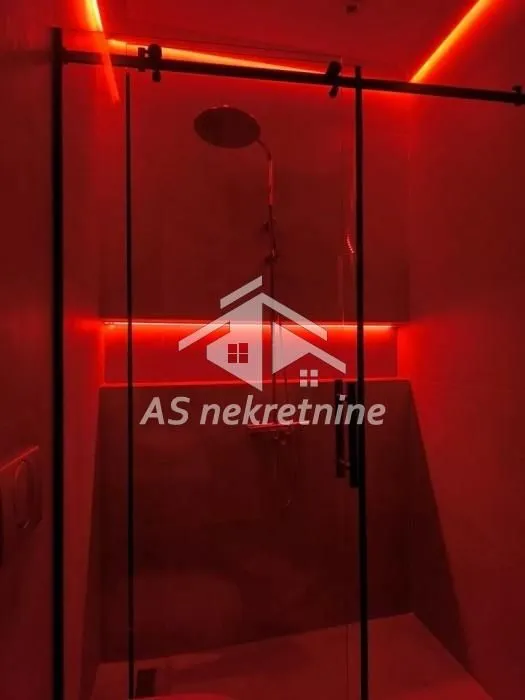 Tuš kabina sa staklenim paravanom i crvenom ambijentalnom rasvjetom.
