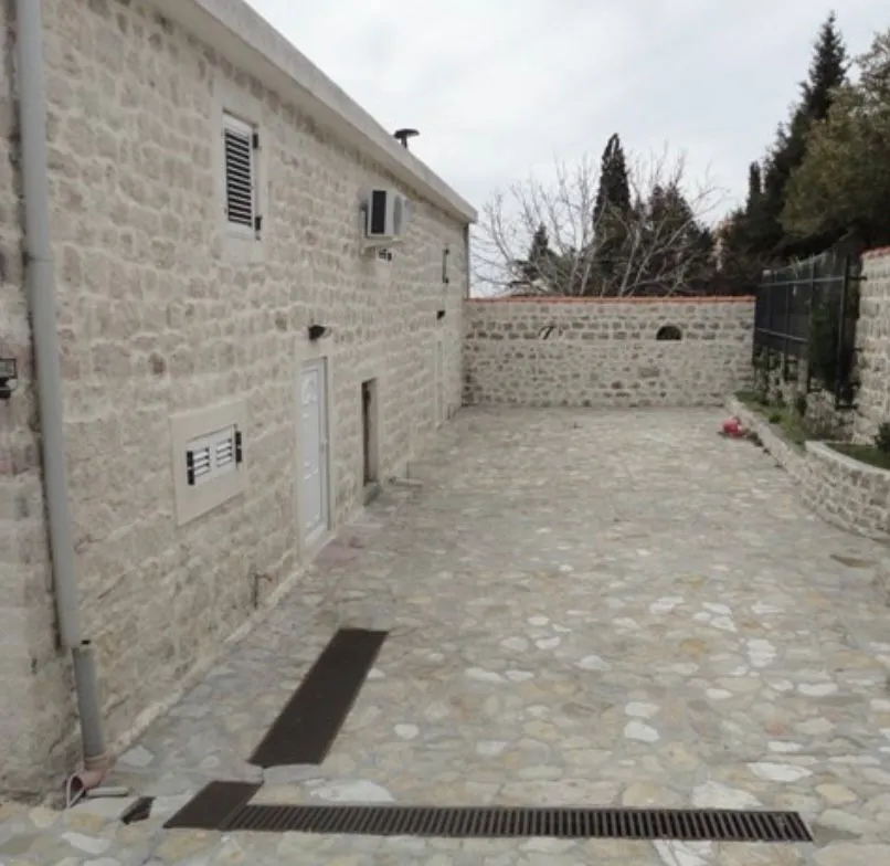 Pogled na popločano dvorište i kamenu fasadu kuće.
