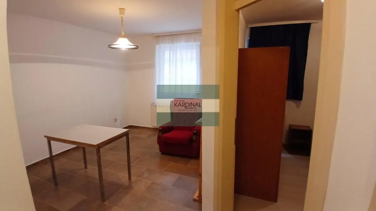 Manja prazna soba sa stolom i crvenom foteljom.