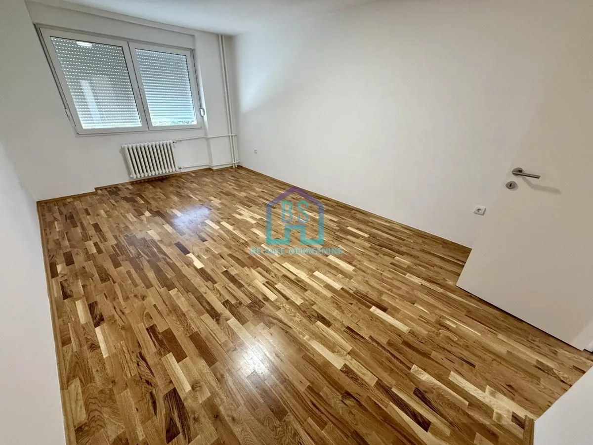 Prazna soba sa parketom i belim zidovima.