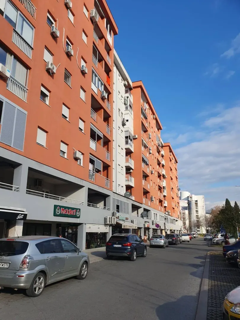 Vanjski izgled višespratne zgrade sa parkiranim automobilima.