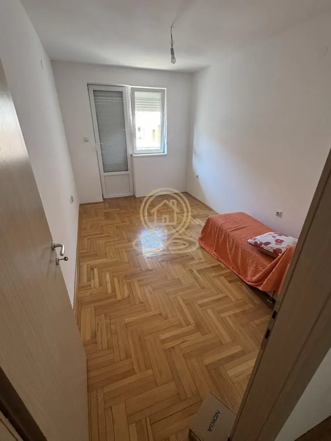 Manja spavaća soba sa krevetom i parketom na podu.
