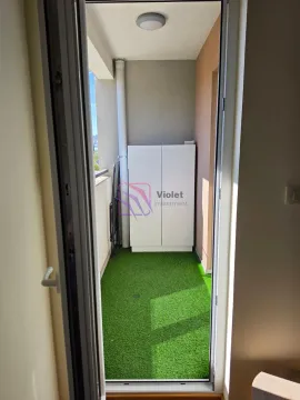 Manji balkon sa vještačkom travom i bijelim ormarićem, viđen kroz otvorena balkonska vrata. - image 13