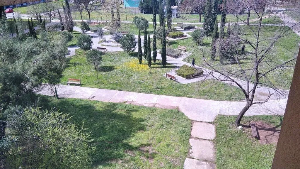 Pogled sa prozora na uređen park i zelene površine.