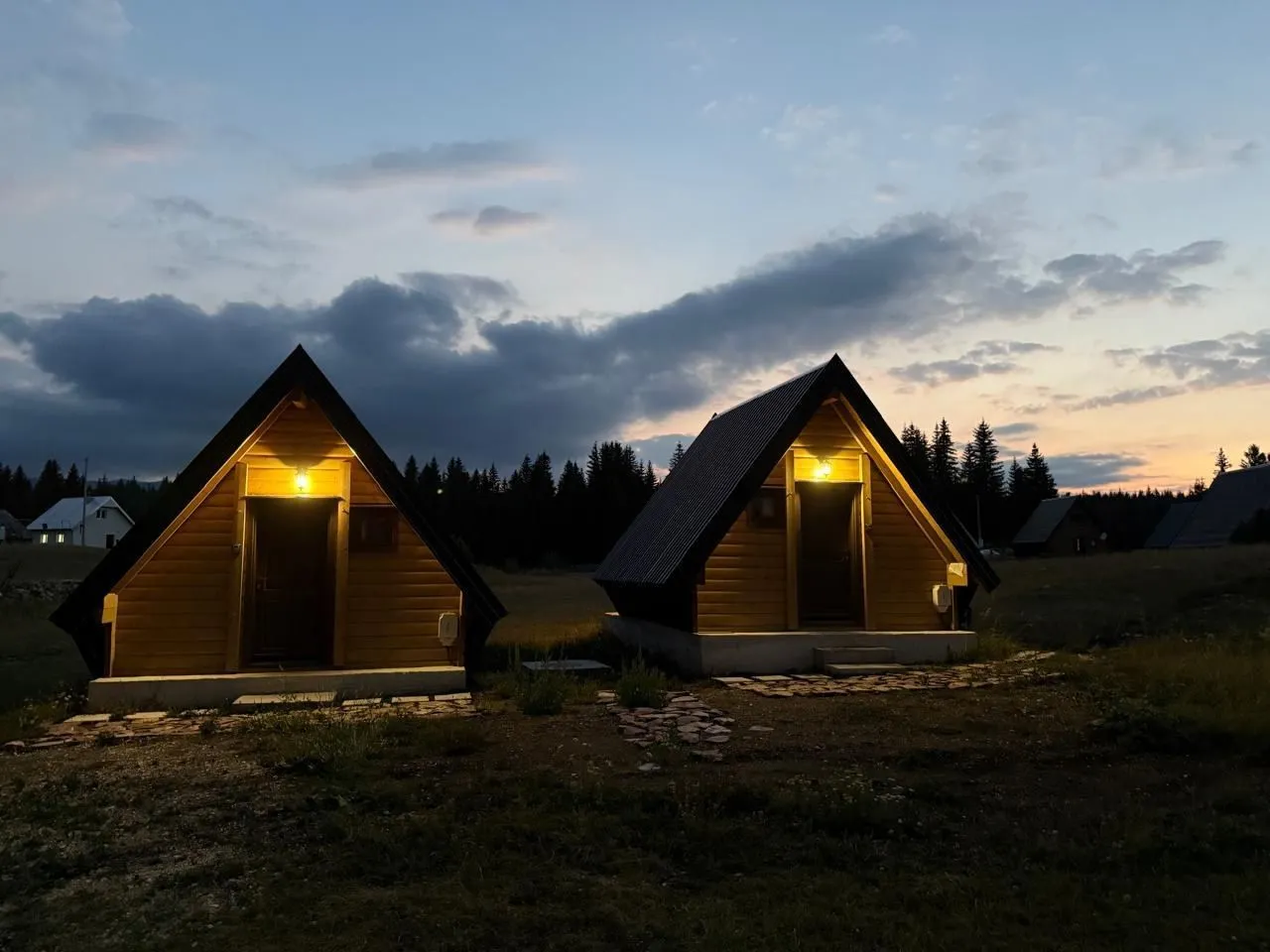 Eksterijer drvenih bungalova u sumrak sa osvijetljenim ulazima.