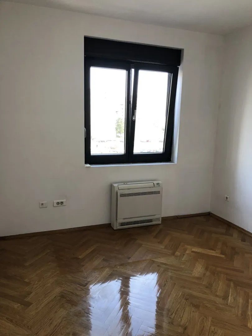Empty room with polished parquet flooring, a window, and a wall-mounted AC unit.