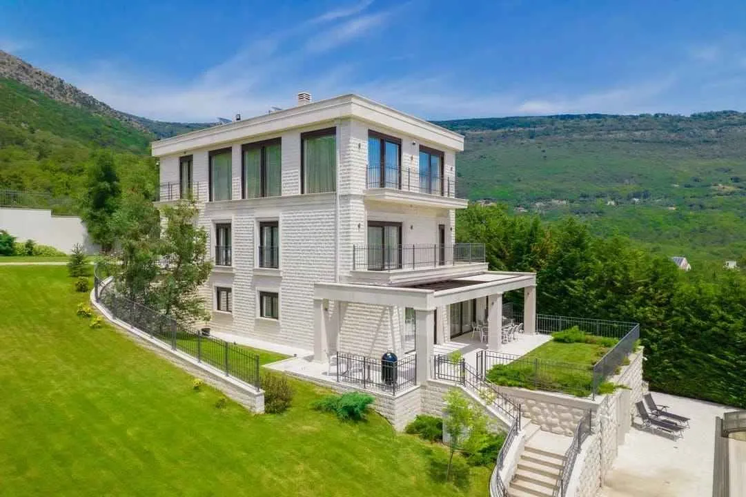 Pogled sa strane na trospratnu vilu sa uređenim dvorištem i terasom.