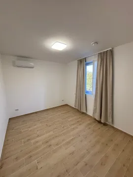 Prazna soba sa bijelim zidovima, drvenim podom, klima uređajem i prozorom sa zavjesama. - image 3