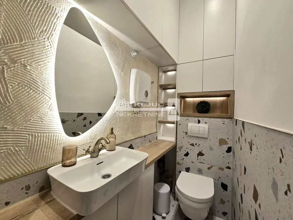 Modern bathroom with a sink, toilet, and illuminated mirror.