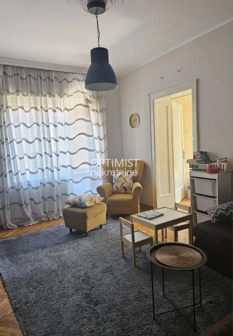 Dnevna soba sa foteljom, stočićem za decu i velikim prozorom.