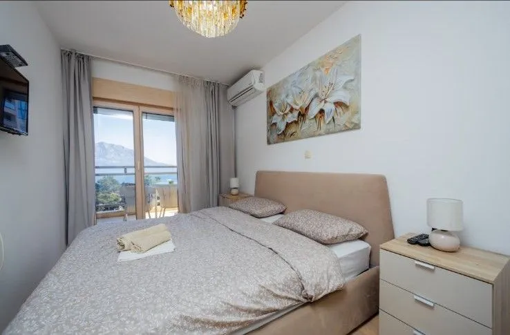 Namještena spavaća soba sa bračnim krevetom, noćnim stolićem i izlazom na terasu.