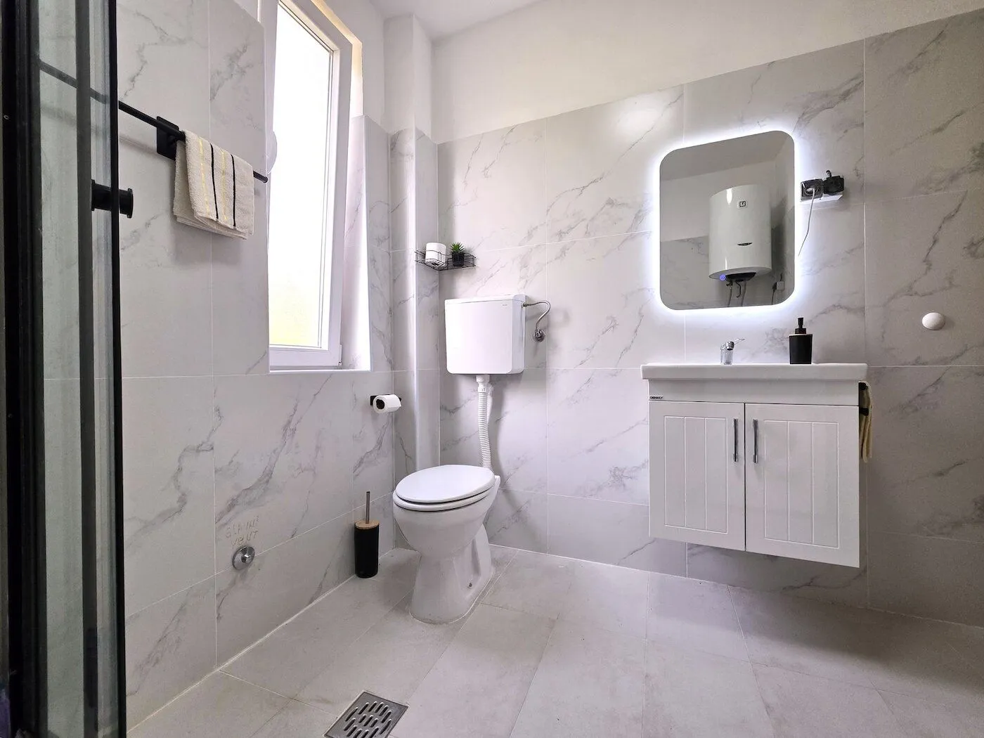 Modern bathroom with white marble tiles, toilet, and vanity unit.