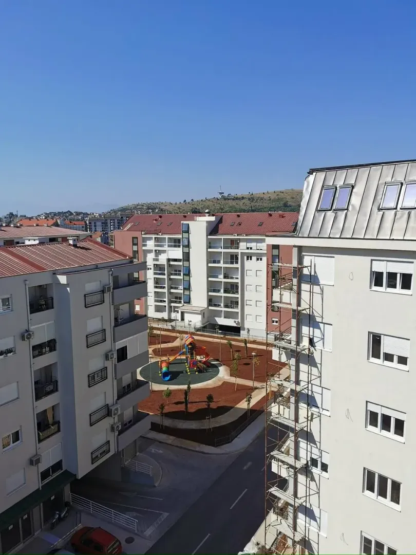 Pogled sa prozora na okolne zgrade i dječije igralište.