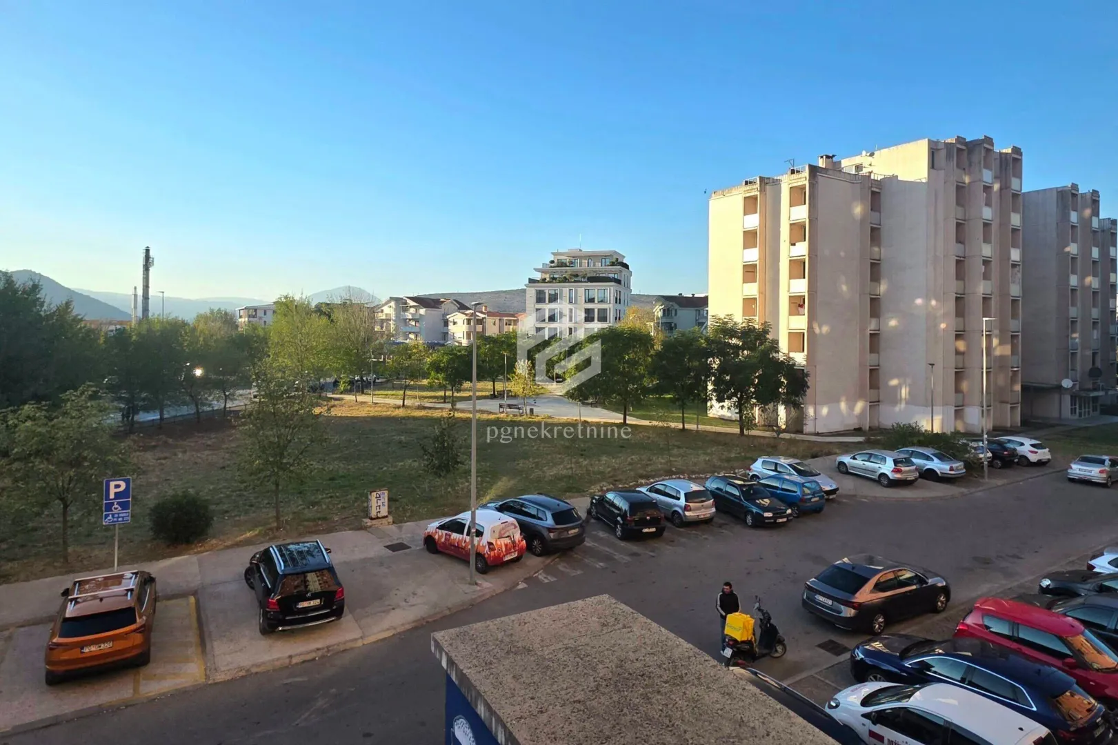 Pogled sa prozora na parking i okolne zgrade.