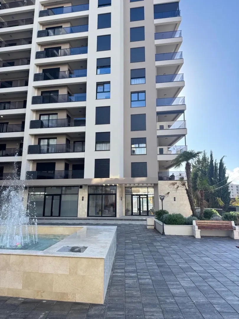 View of the facade of a modern multi-story building with a fountain and landscaped courtyard.