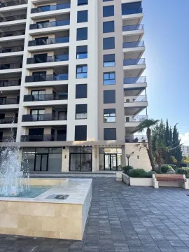 View of the facade of a modern multi-story building with a fountain and landscaped courtyard. - image 8