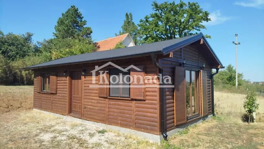 Eksterijer prizemne drvene vikendice sa dvorištem i zelenilom u okruženju.