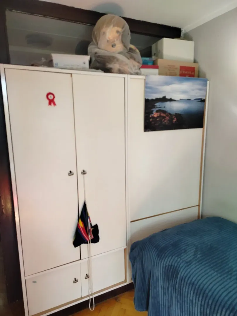 Spavaća soba sa bijelim ormarom pored kreveta sa plavim prekrivačem.