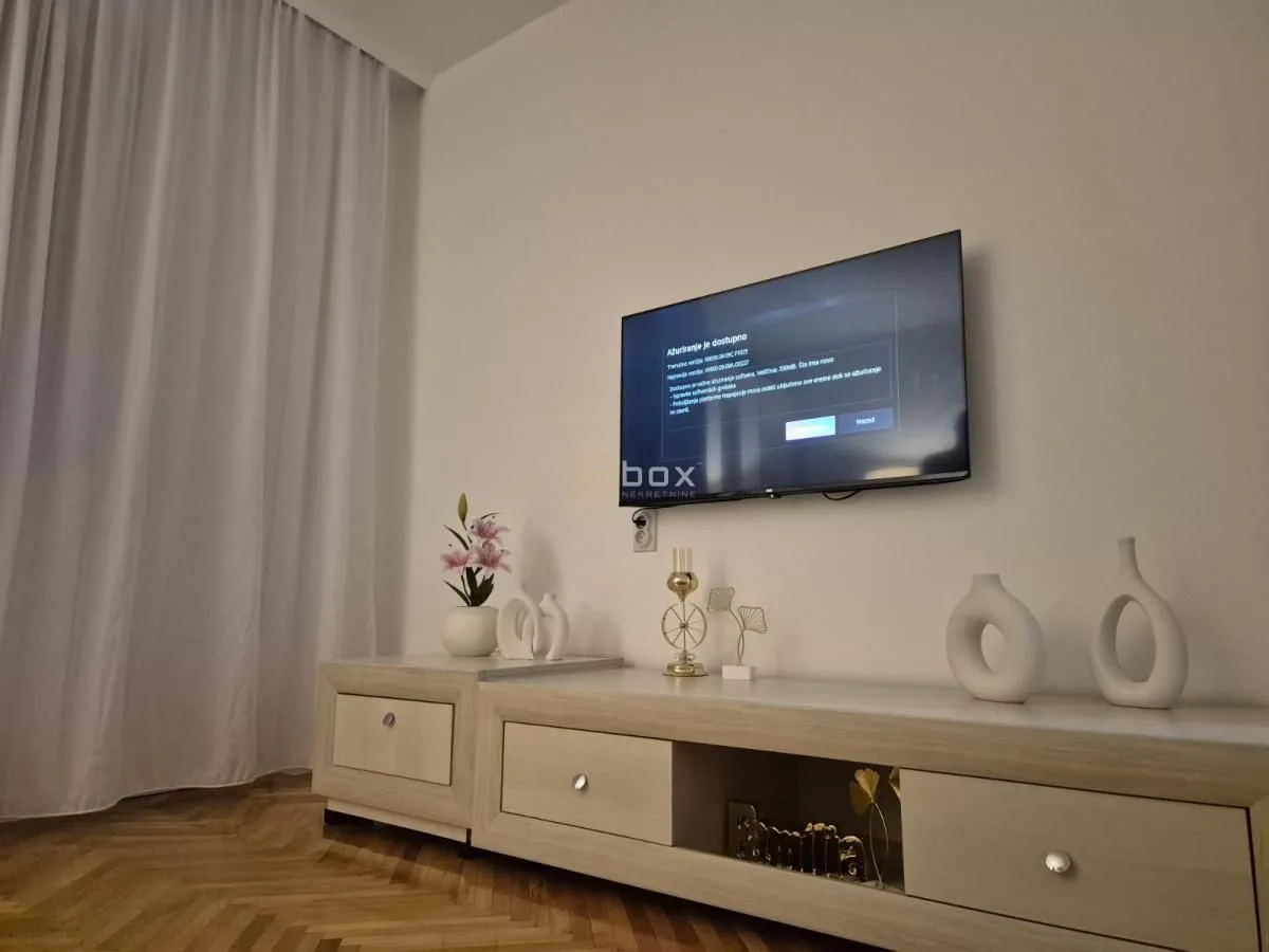 Dnevna soba sa televizorom na zidu i komodom ispod.