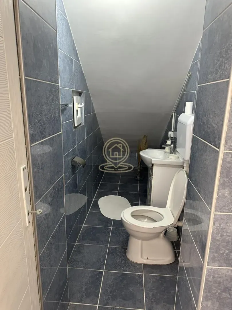 Manje kupatilo obloženo tamnim pločicama sa kosim plafonom i sanitarijama.