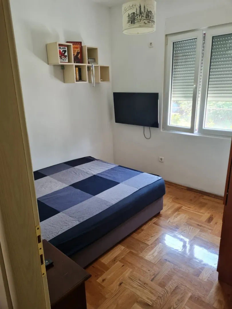 A simply furnished bedroom with a TV and parquet flooring.