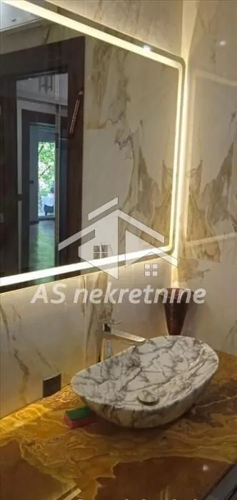 Kupatilo sa mermernim umivaonikom i osvetljenim ogledalom.