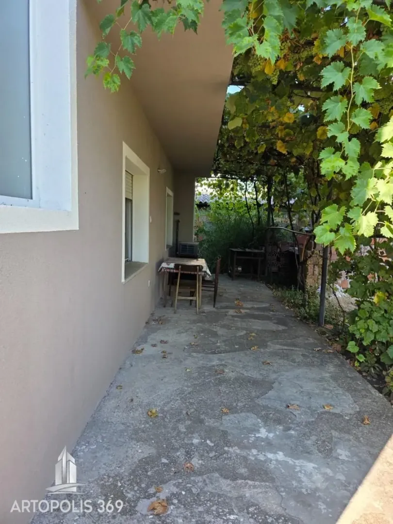 Covered terrace in front of the house with a table and greenery.