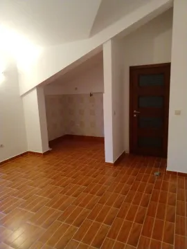 Prazna prostorija sa pločicama na podu, kosim plafonom i drvenim vratima. - image 3
