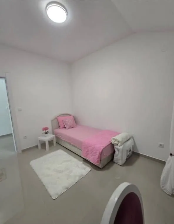 Manja spavaća soba sa jednim krevetom i roze posteljinom.
