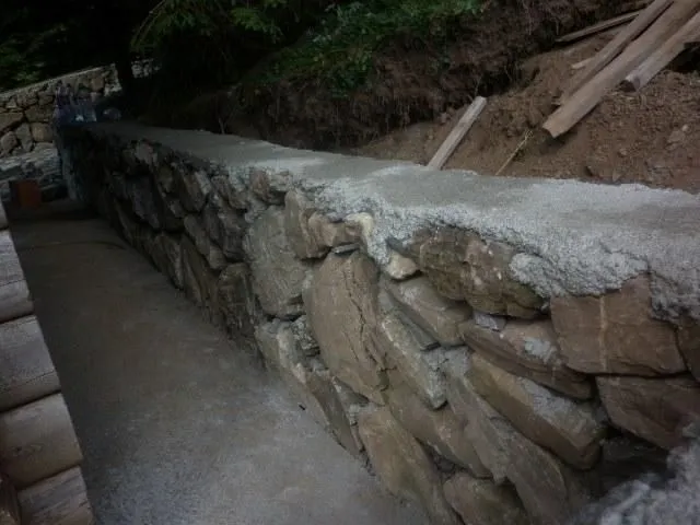 Kameni potporni zid pored betonske staze u dvorištu.