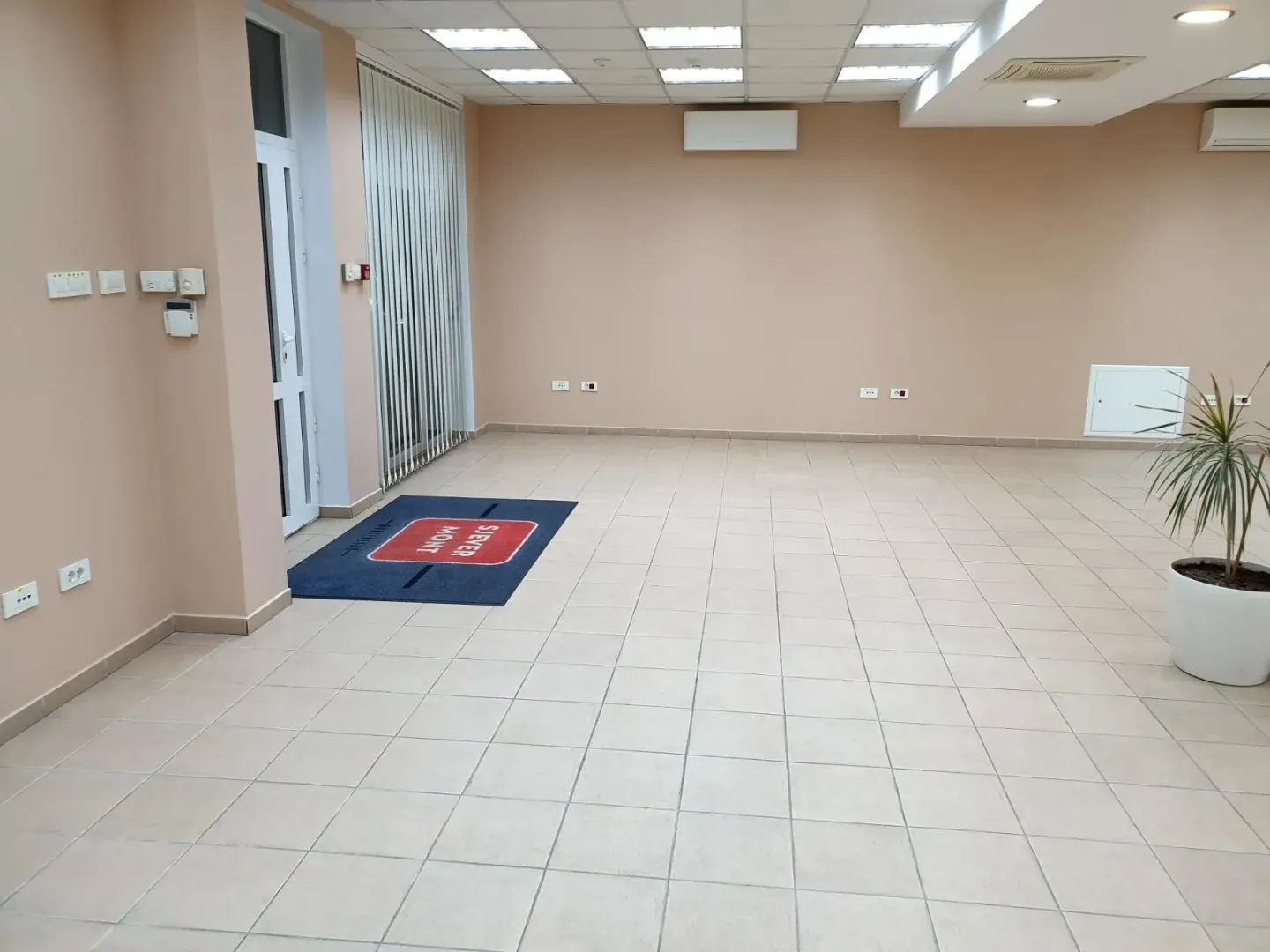 Empty commercial space with light tiled flooring and beige walls.