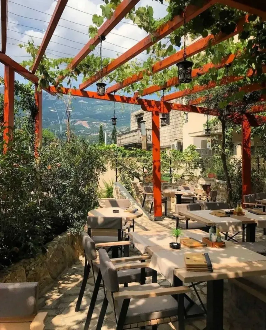 Outdoor restaurant terrace with a wooden pergola covered in vines and set tables.