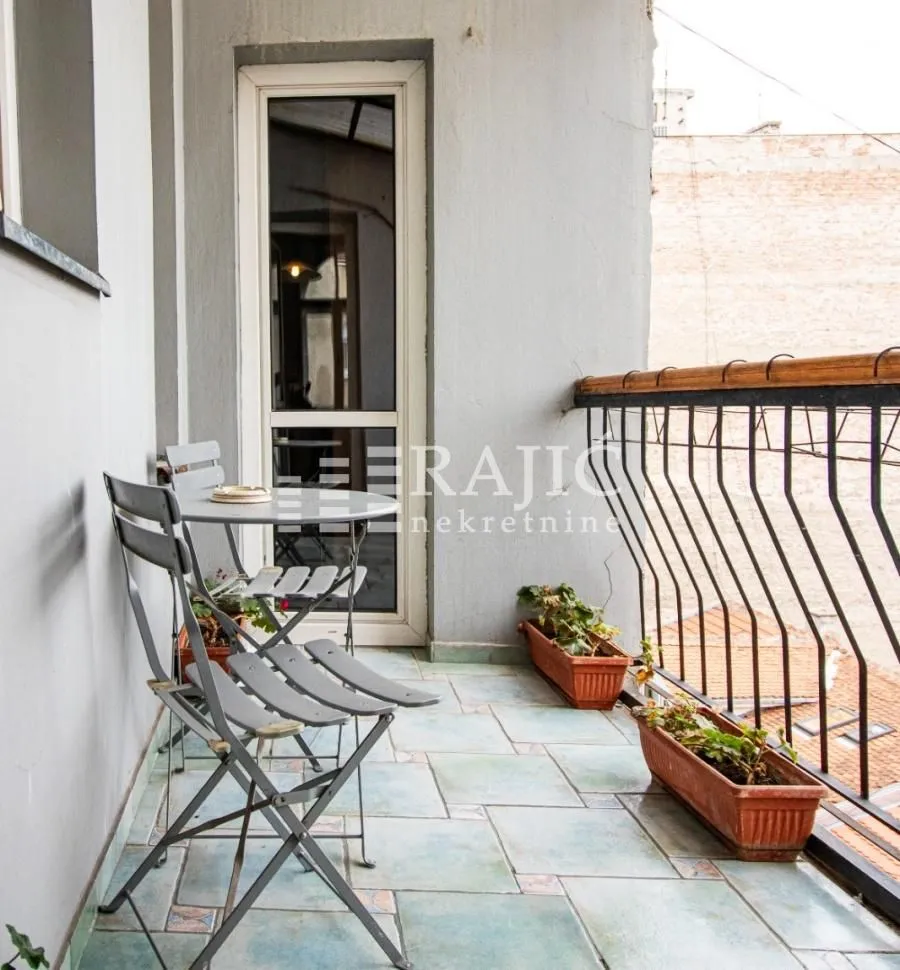 Small enclosed balcony with a table, chairs, and flowers.