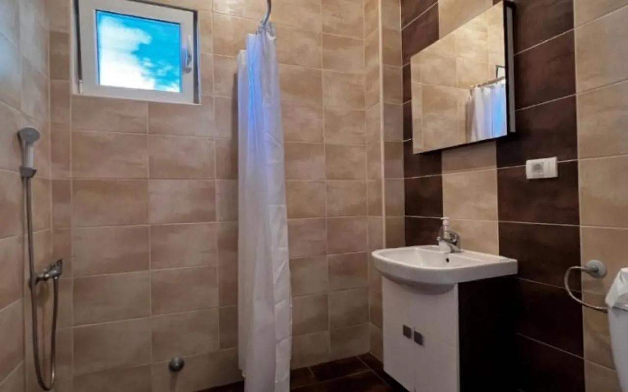 Kupatilo sa tuš kabinom, umivaonikom i ogledalom obloženo keramičkim pločicama.