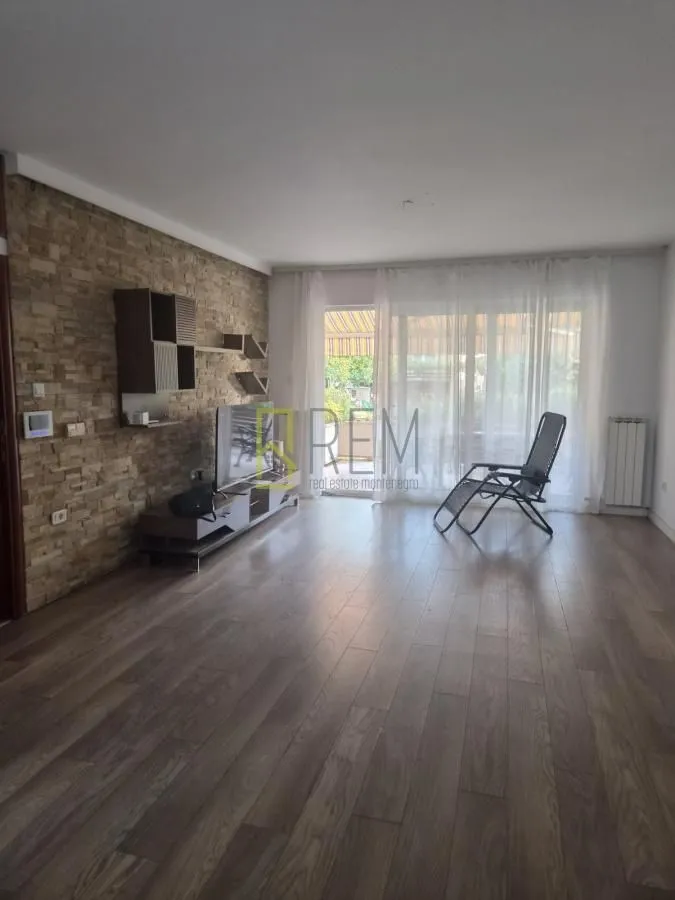 Living room with wooden flooring, stone wall, and access to the terrace.