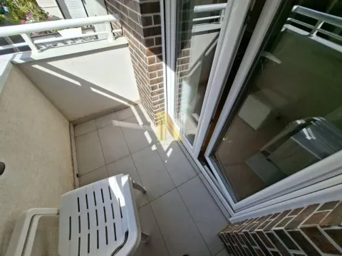 Manji popločani balkon sa belom plastičnom stolicom i balkonskim vratima. - image 10