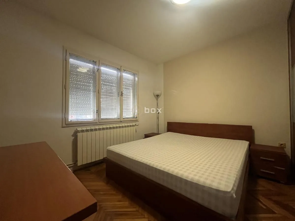 Nameštena spavaća soba sa bračnim krevetom, prozorom i drvenim podom.